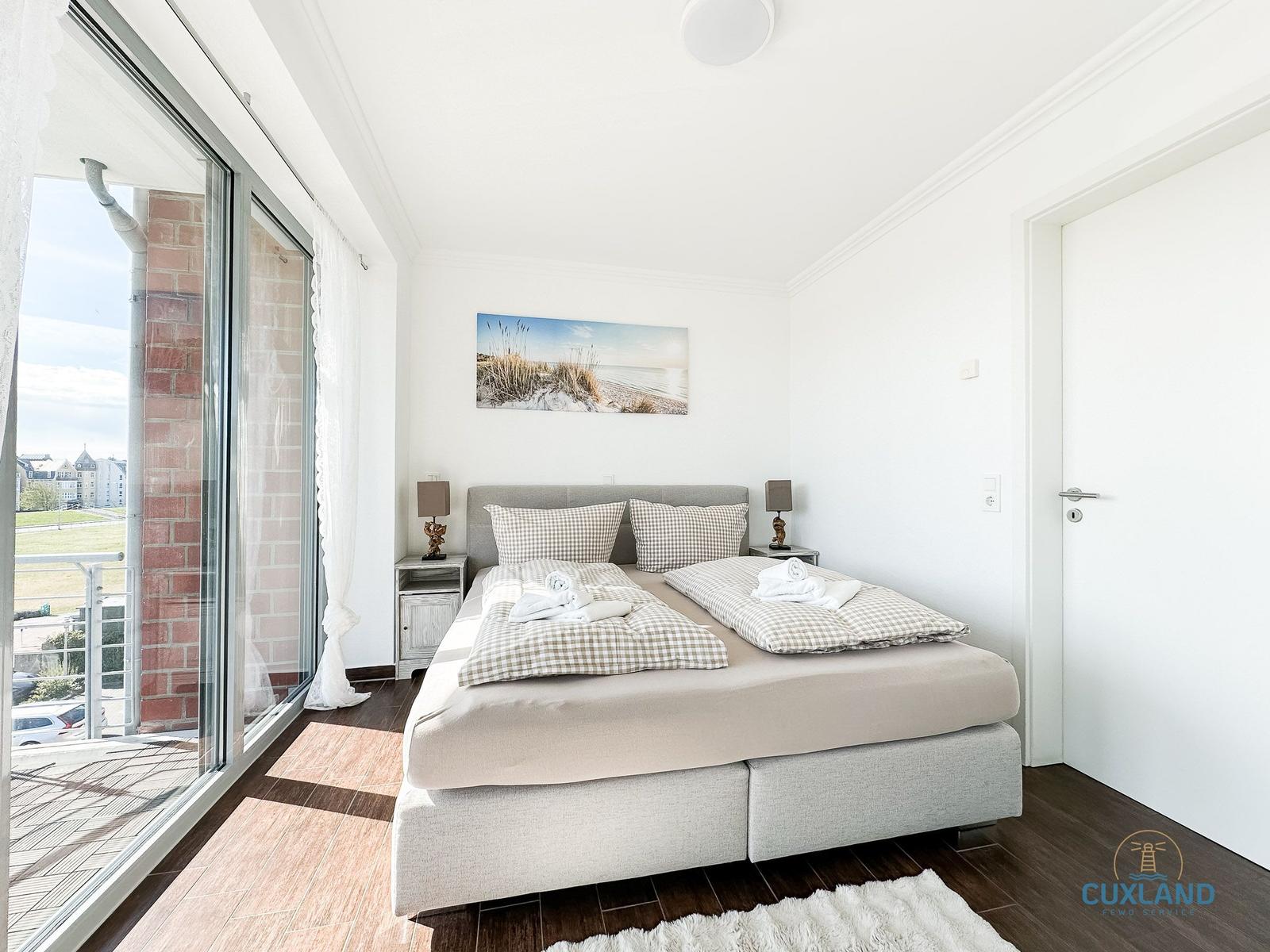 Schlafzimmer mit Doppelbett, Balkon und Wandbild. Holzboden und weiße Wände.