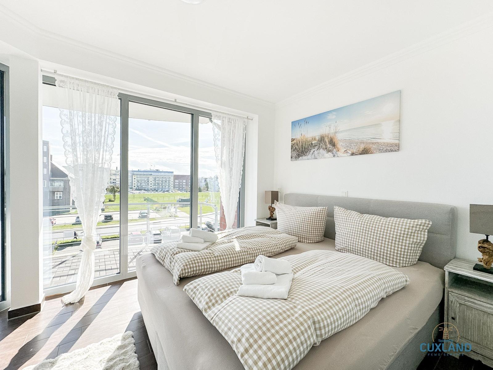 Schlafzimmer mit Doppelbett, Blick auf Balkon und Stadt. Wandbild und Nachttische.