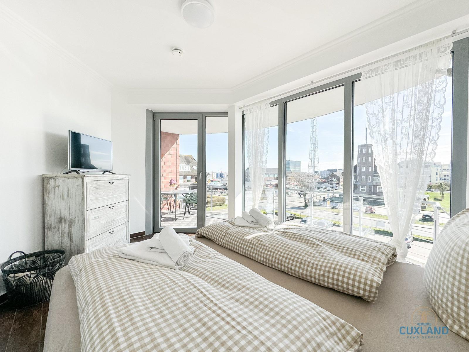 Zwei Betten mit karierten Bettdecken, Fernseher und großes Fenster mit Blick auf die Stadt.