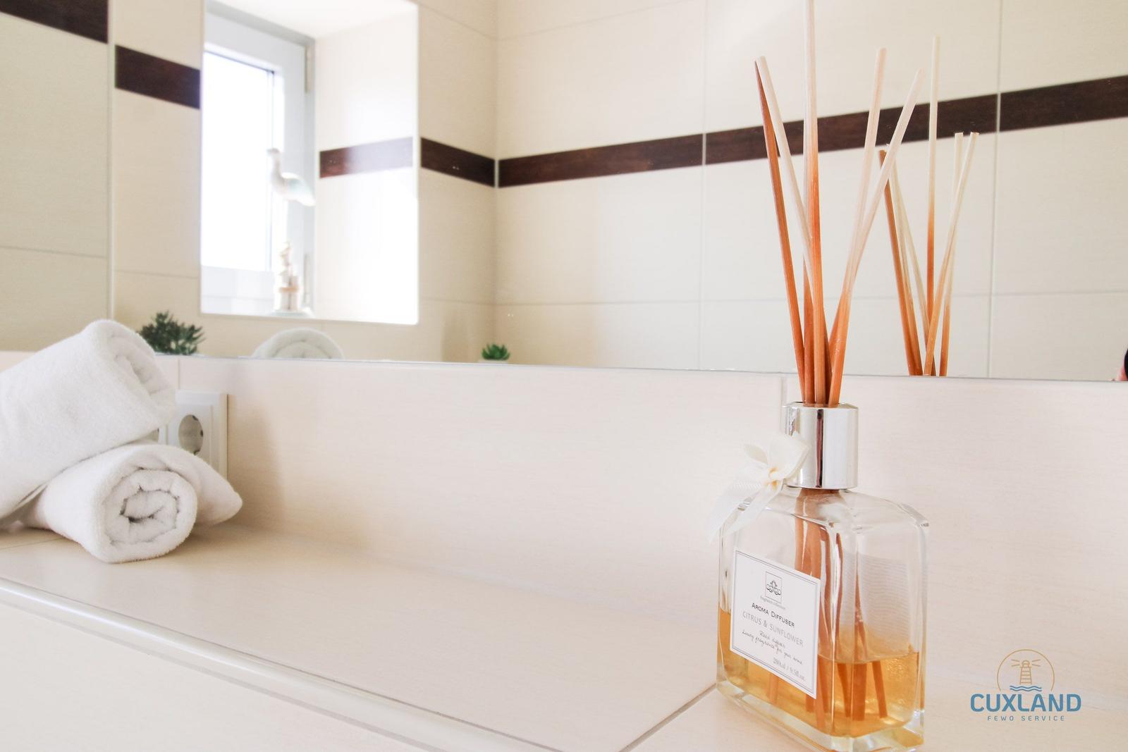 Badezimmer mit Spiegel, Handtuch und Duftdiffusor auf Waschtisch.