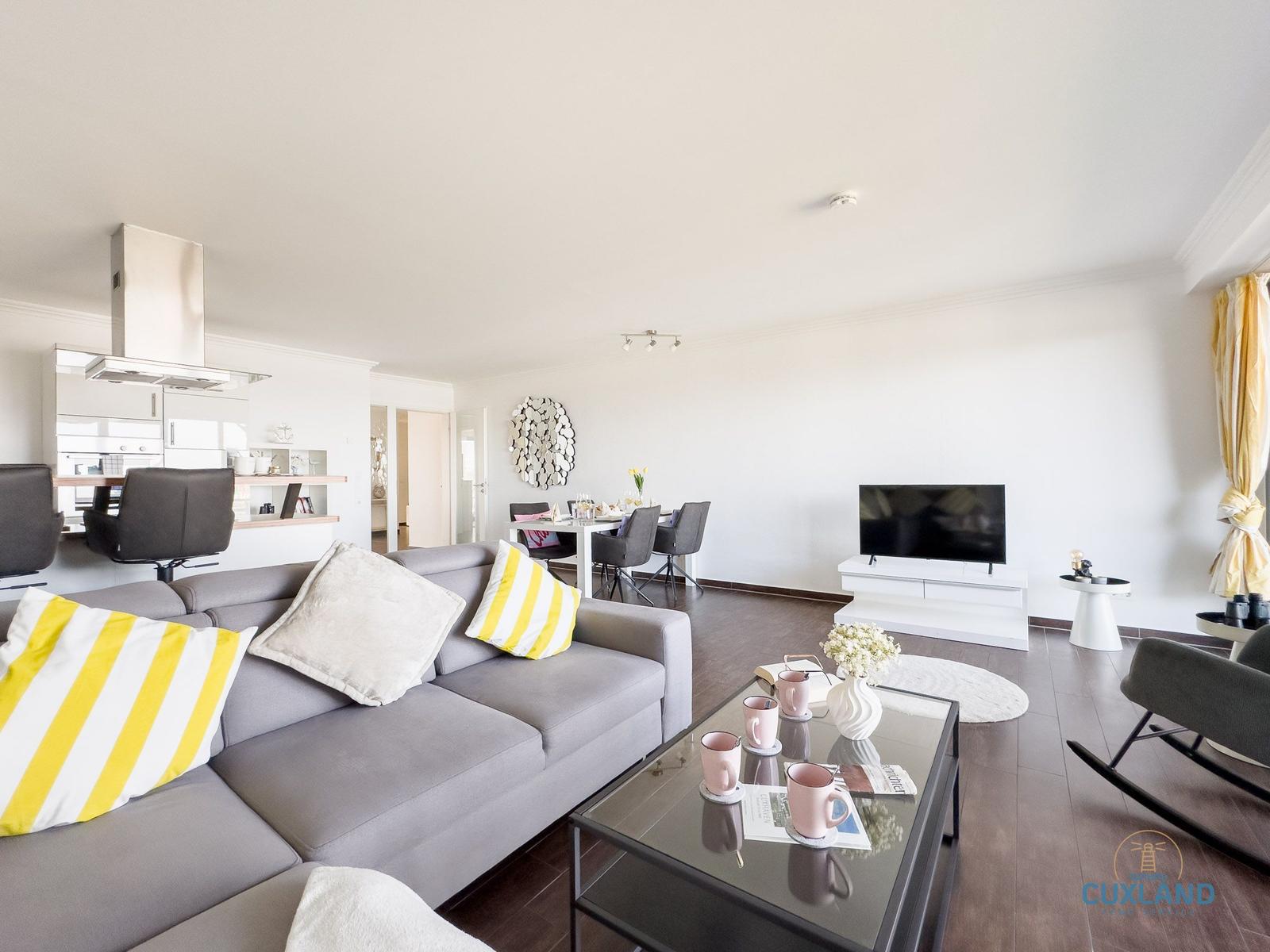 Wohnzimmer mit Sofa, Esstisch und Küche im Hintergrund.