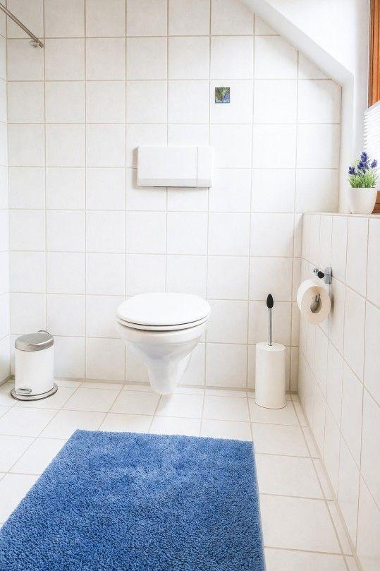 Badezimmer mit Toilette, blauem Teppich und weißen Fliesen