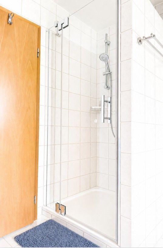 Dusche mit Glaswand, weißen Fliesen und blauem Teppich vor der Tür.