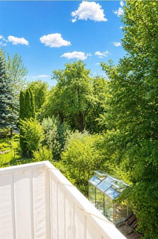 Blick von Balkon auf grüne Bäume und einen Gewächshaus unter blauem Himmel.