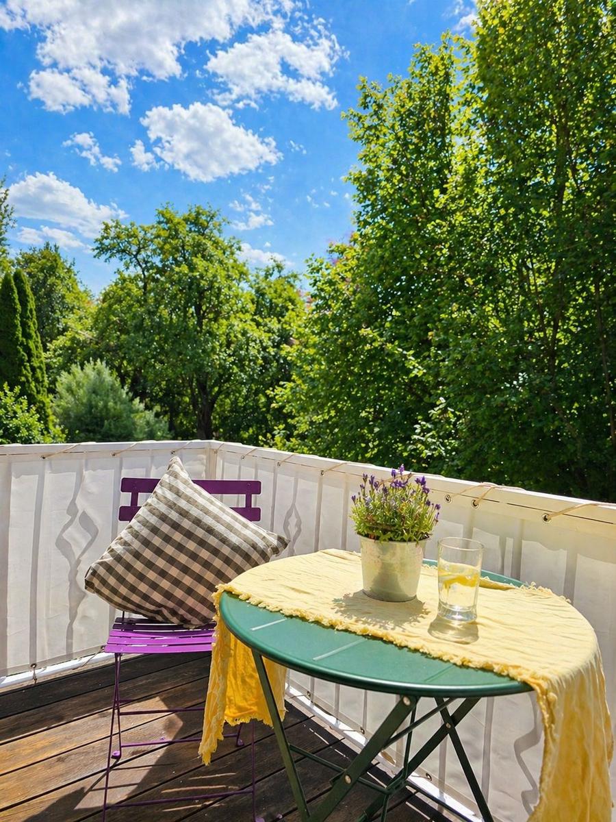 Terrasse mit Tisch, Stuhl und Pflanze. Hintergrund: grüne Bäume und blauer Himmel.
