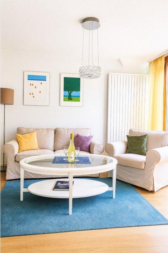 Wohnzimmer mit Sofa, Sessel und runden Tisch auf blauem Teppich.