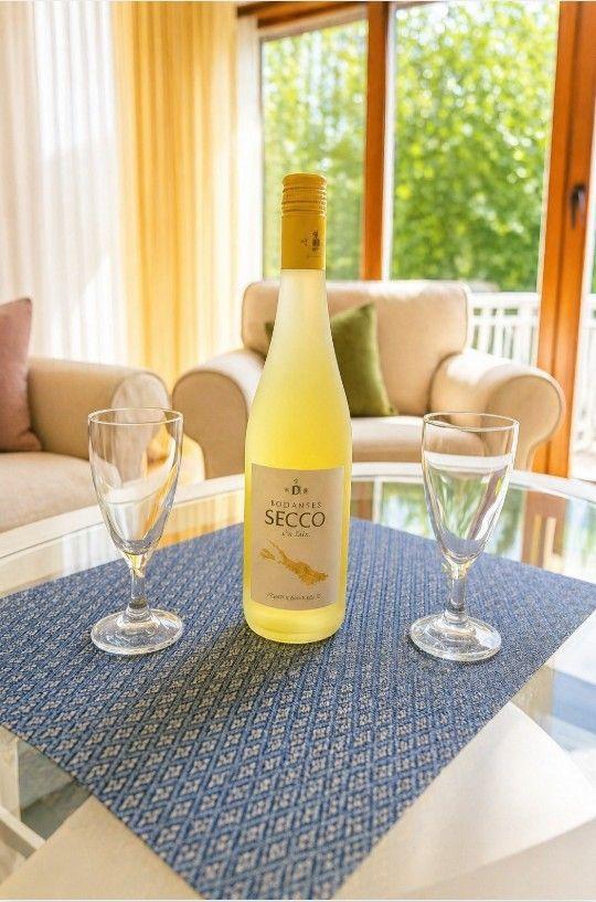 Eine Flasche Weißwein und zwei Gläser stehen auf einem Tisch vor einem Fenster mit Blick auf eine Terrasse.