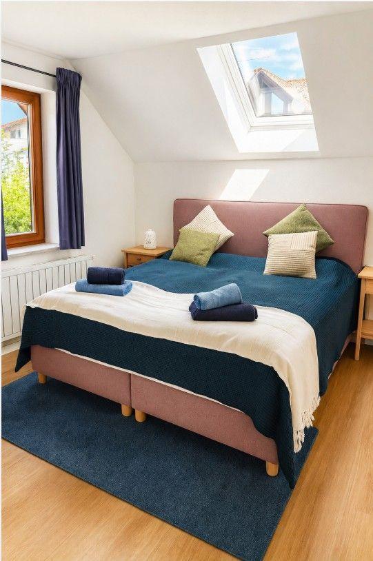 Schlafzimmer mit Dachschrägen, Fenster und Dachfenster. Bett mit Decke und Kissen.