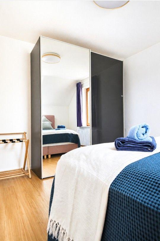 Schlafzimmer mit Bett, Spiegelschrank und Holzboden. Handtuch auf Bett.