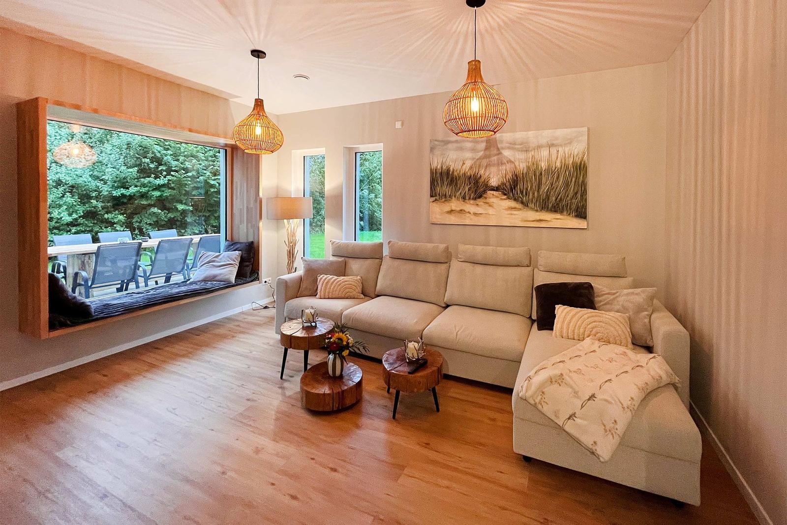 Wohnzimmer mit Sofa, Fensterbank und Holzboden. Deckenleuchten und Wandbild.