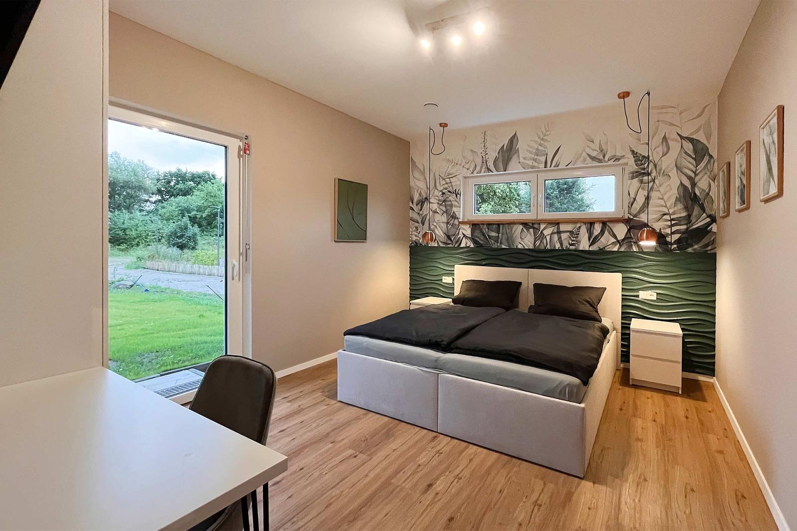 Schlafzimmer mit Doppelbett, grünem Wandpaneel und Fenster zur grünen Außenseite.