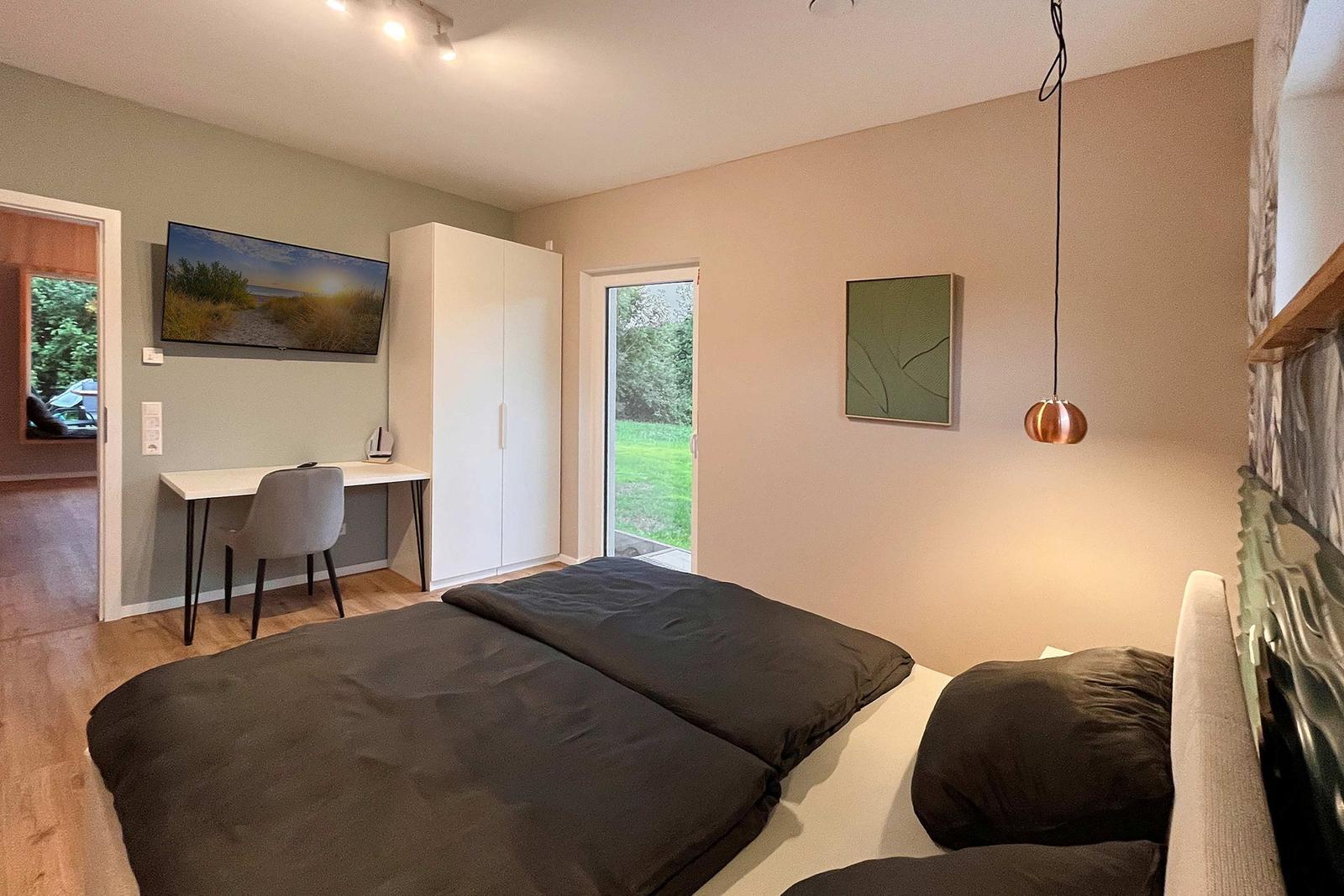 Schlafzimmer mit Bett, Schreibtisch, Kleiderschrank und Fenster zum Garten.