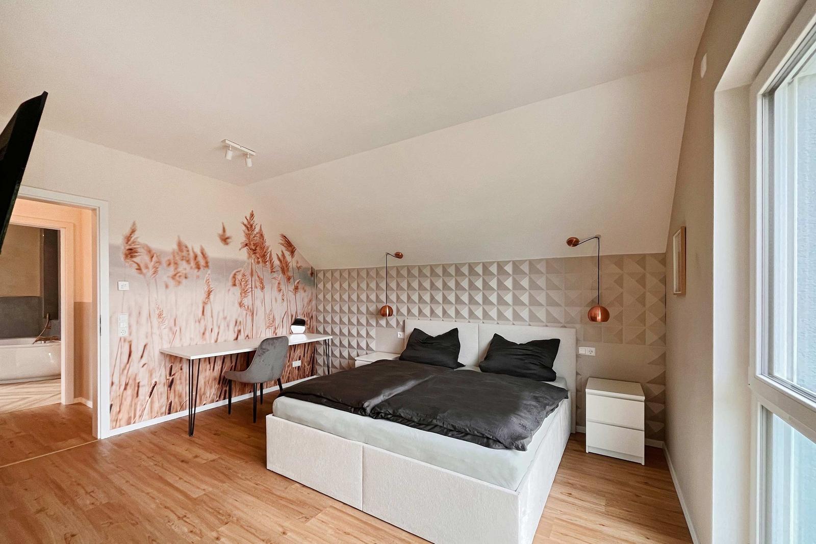 Schlafzimmer mit Bett, Schreibtisch und Wandbild. Durchgang zur Badewanne.