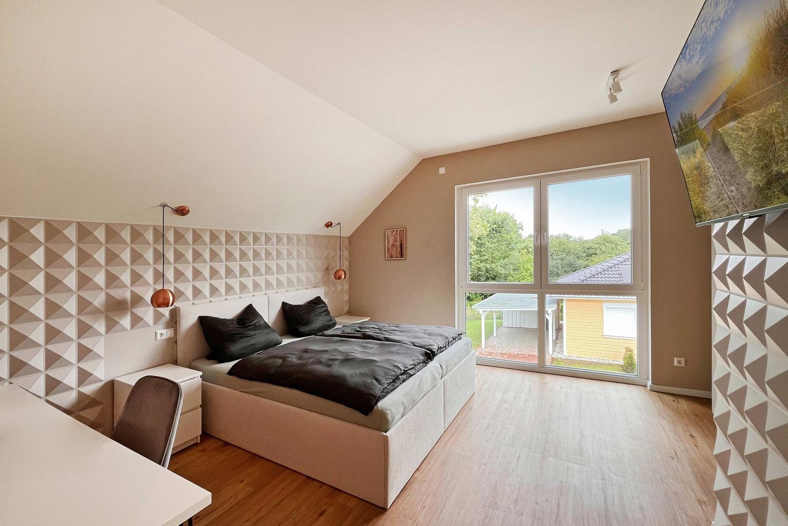 Schlafzimmer mit Doppelbett, Schreibtisch und Fenster zur Außenseite.