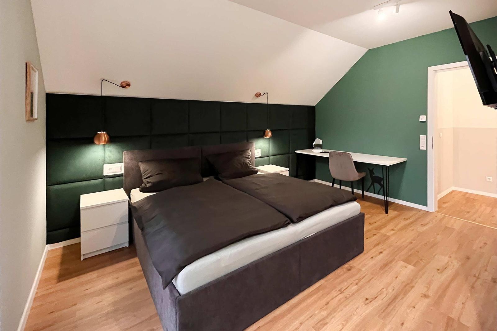 Schlafzimmer mit Doppelbett, Schreibtisch und Fernseher an der Wand.