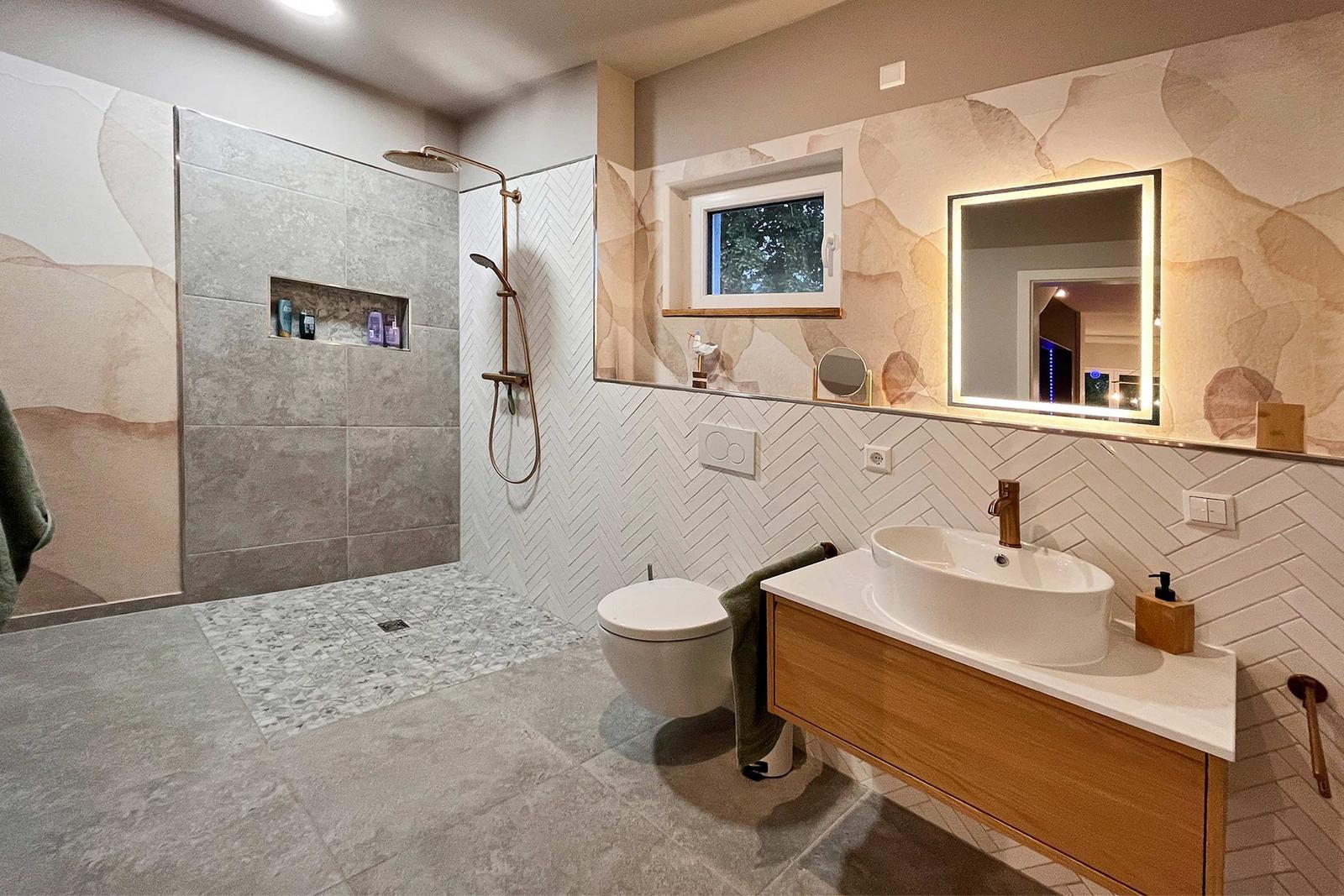 Badezimmer mit Dusche, Waschbecken und Toilette. Helle Fliesen und Holzakzente.