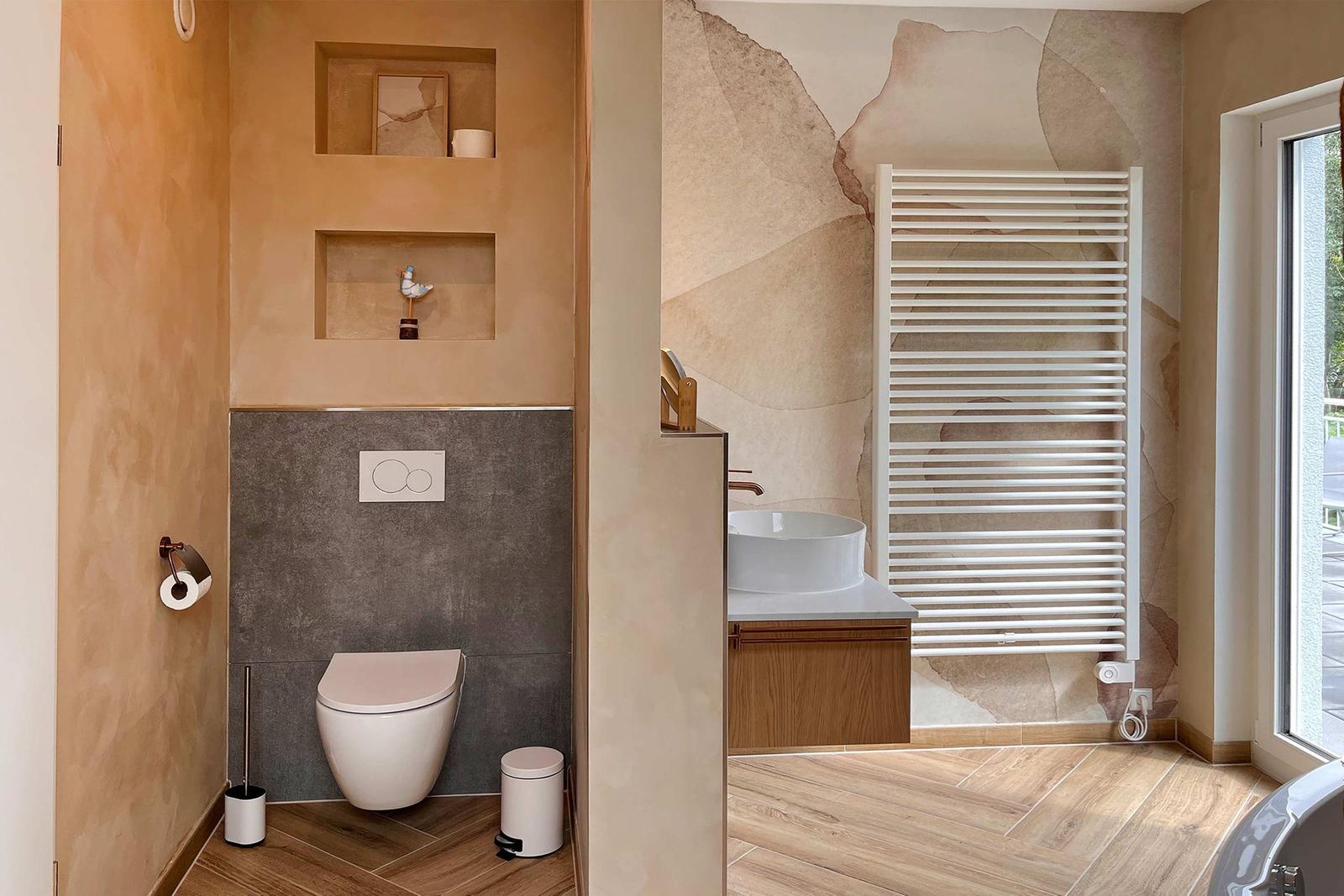 Badezimmer mit Toilette, Waschbecken und Heizkörper. Holzfußboden und Wanddekoration.