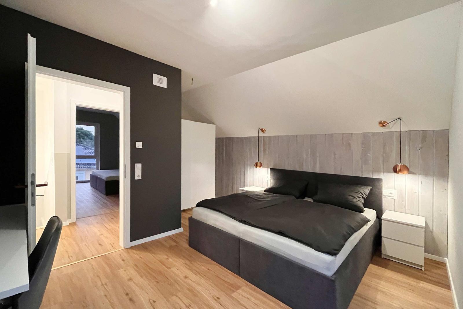 Schlafzimmer mit Bett, Nachttischen und Tür zum angrenzenden Raum.