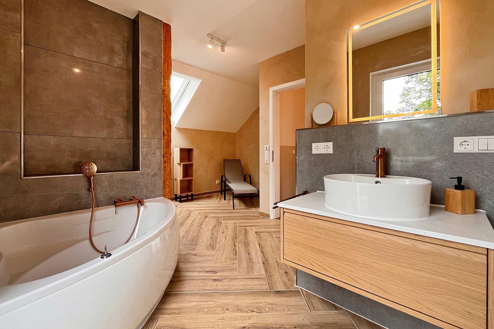 Bad mit freistehender Badewanne, Waschtisch und Dusche. Holzboden und warme Wände.