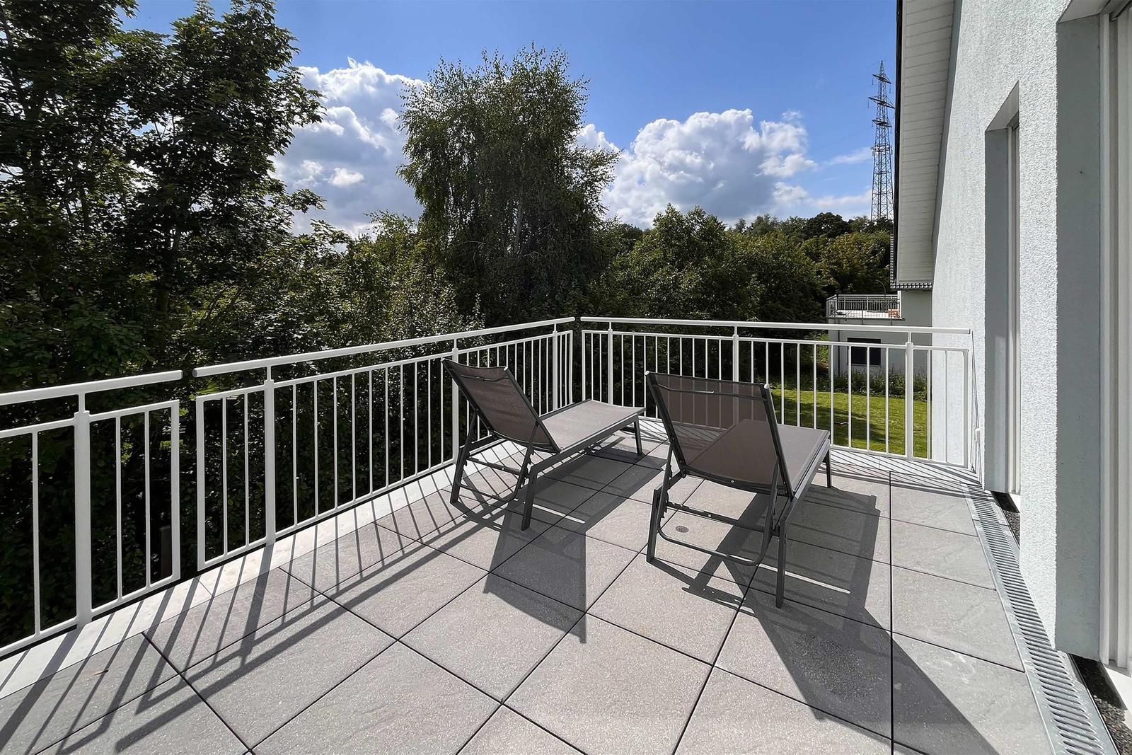 Terrasse mit zwei Liegestühlen, Blick auf Bäume und Himmel.
