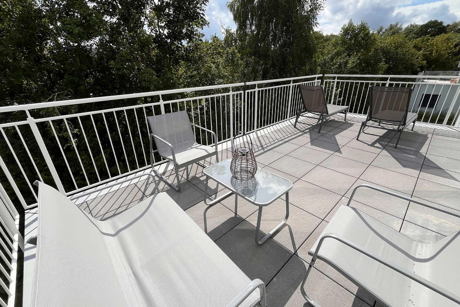 Terrasse mit Liegestühlen und Tisch. Blick auf grüne Bäume und Himmel.