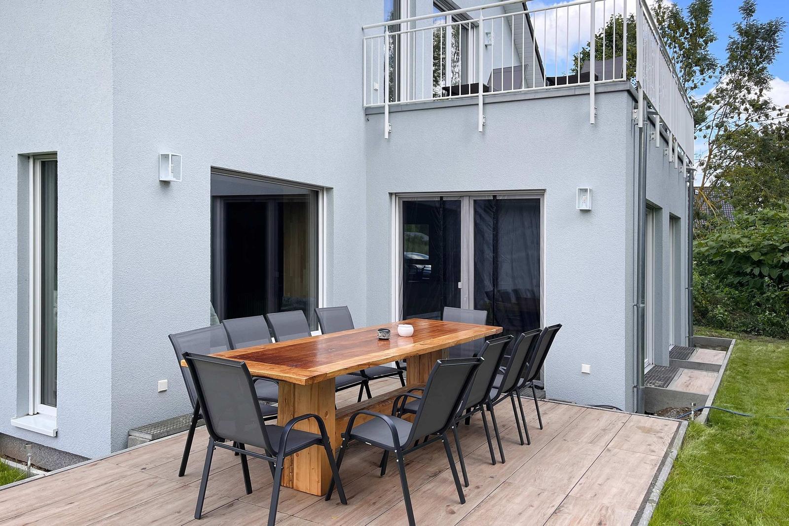 Terrasse mit Holztisch und acht Stühlen vor modernem Haus mit Balkon.