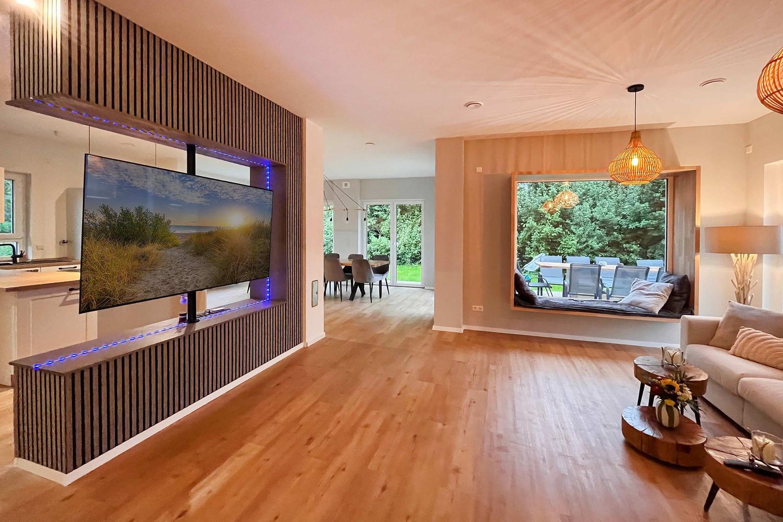Wohnbereich mit TV, Sofa und Blick auf Garten. Holzboden und modern eingerichtet.