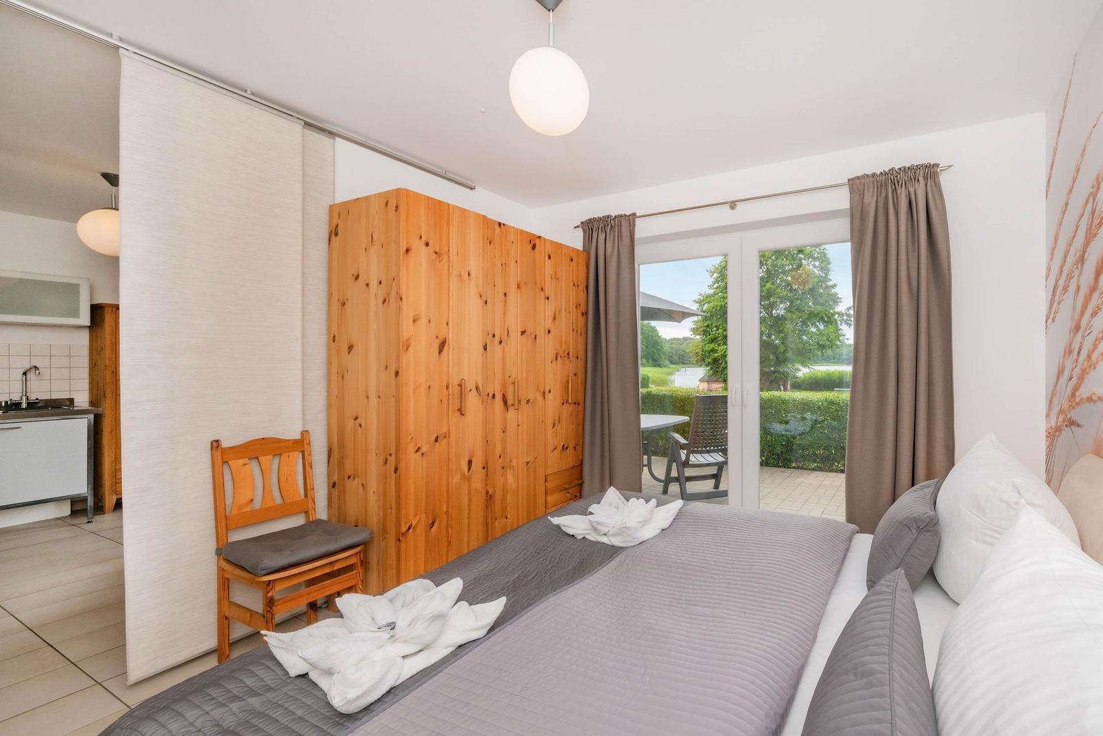 Schlafzimmer mit Bett, Holzschrank und Blick auf Balkon mit Garten.