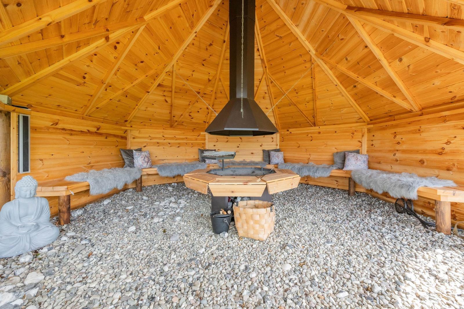 Holzsauna mit Kamin, Sitzbänken und Buddha-Statue auf Kiesboden.