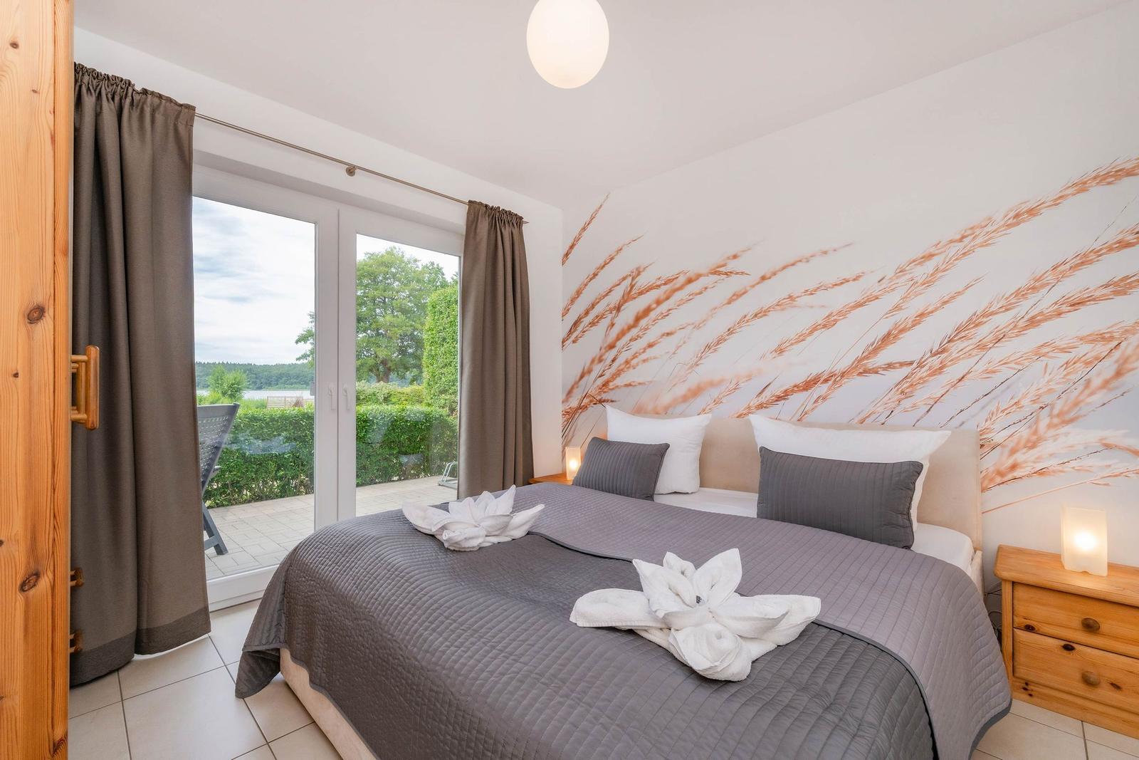 Schlafzimmer mit Bett, Wandbild und Terrasse. Blick auf Garten und See.