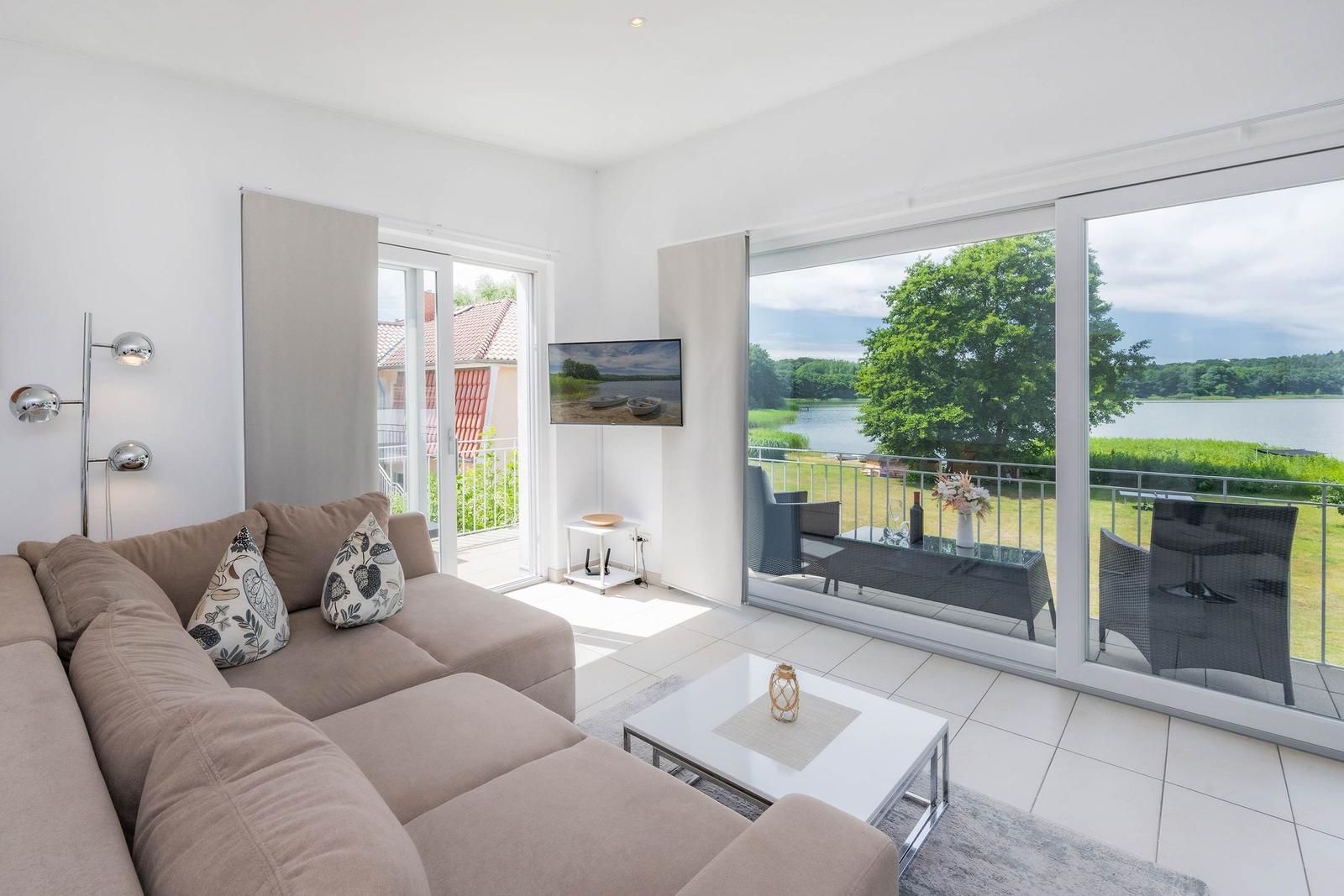 Wohnzimmer mit Sofa, TV und Blick auf einen See.