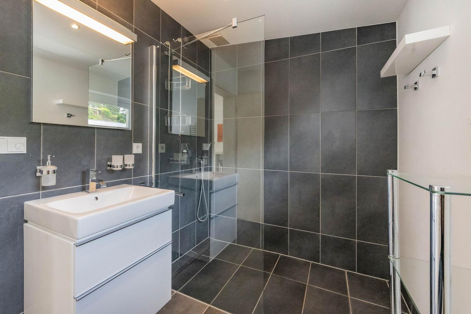 Badezimmer mit Dusche, Waschbecken und Spiegel. Fliesen an Wänden und Boden.