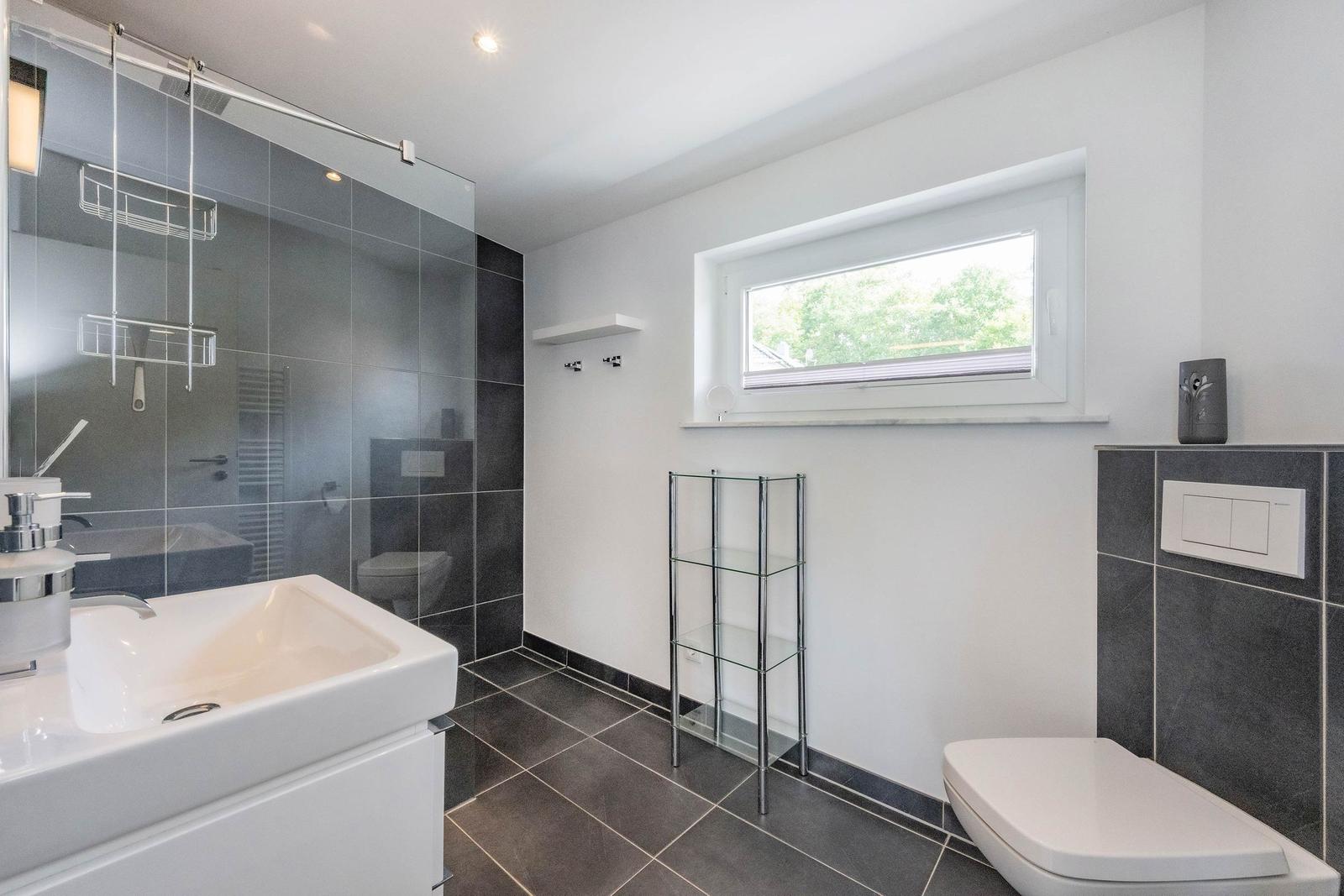 Bad mit Dusche, Waschbecken und Toilette. Fenster mit Blick auf Grün.