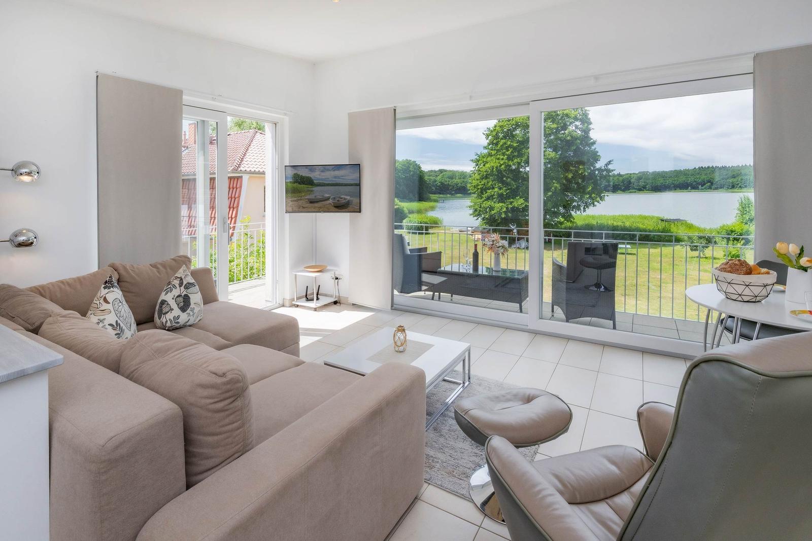 Wohnzimmer mit Sofa, Fernseher und Blick auf den See.