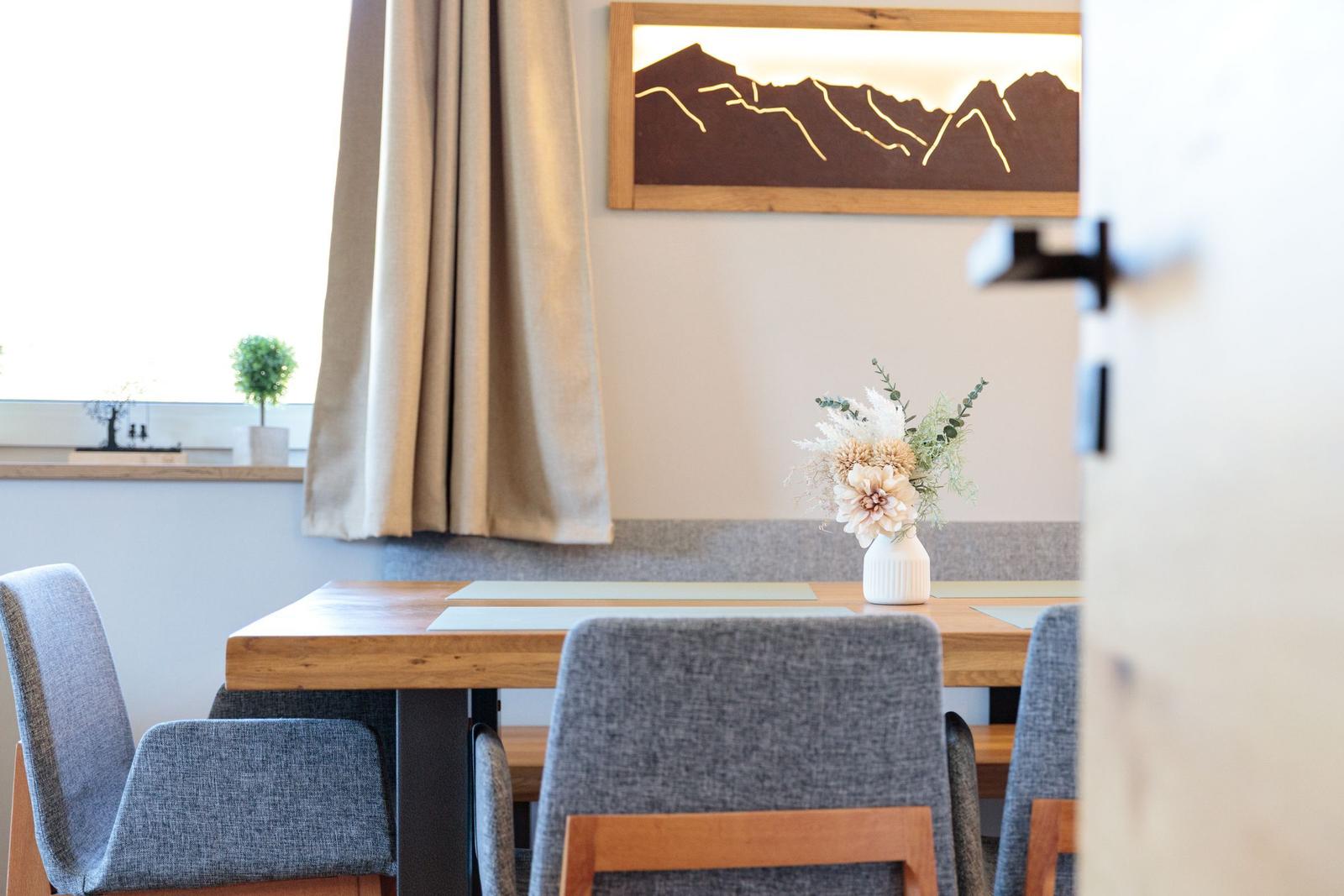 Essbereich mit Holztisch, grauen Stühlen und Wandbild mit Bergmotiv.