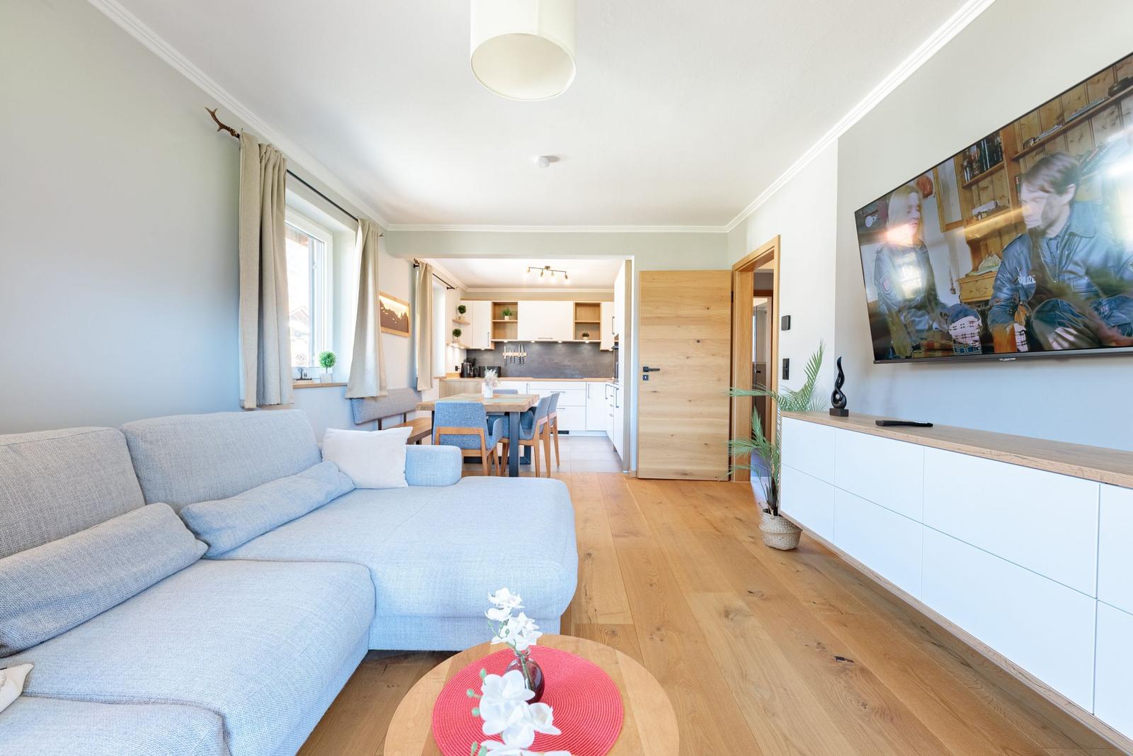 Wohnzimmer mit Sofa, TV und Küchenbereich im Hintergrund.
