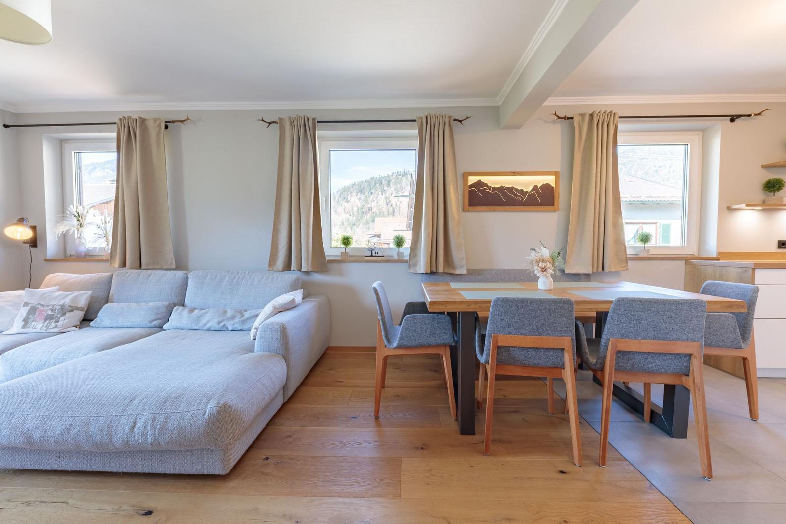 Wohn- und Essbereich mit Sofa, Tisch und Stühlen. Fenster mit Blick auf Berge.