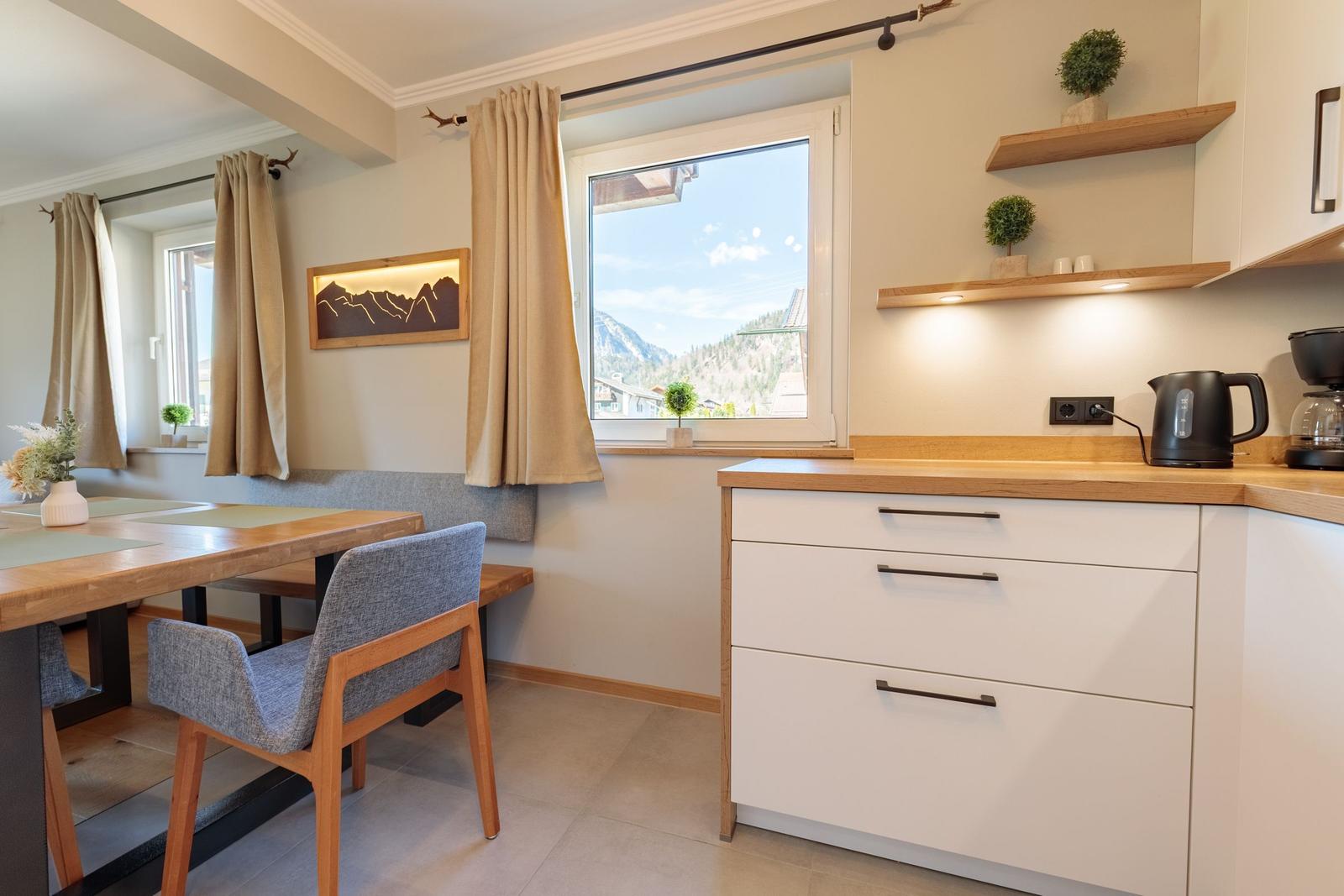 Küche mit Essbereich, Fensterblick auf Berge, Holztische, Stühle und Schränke.