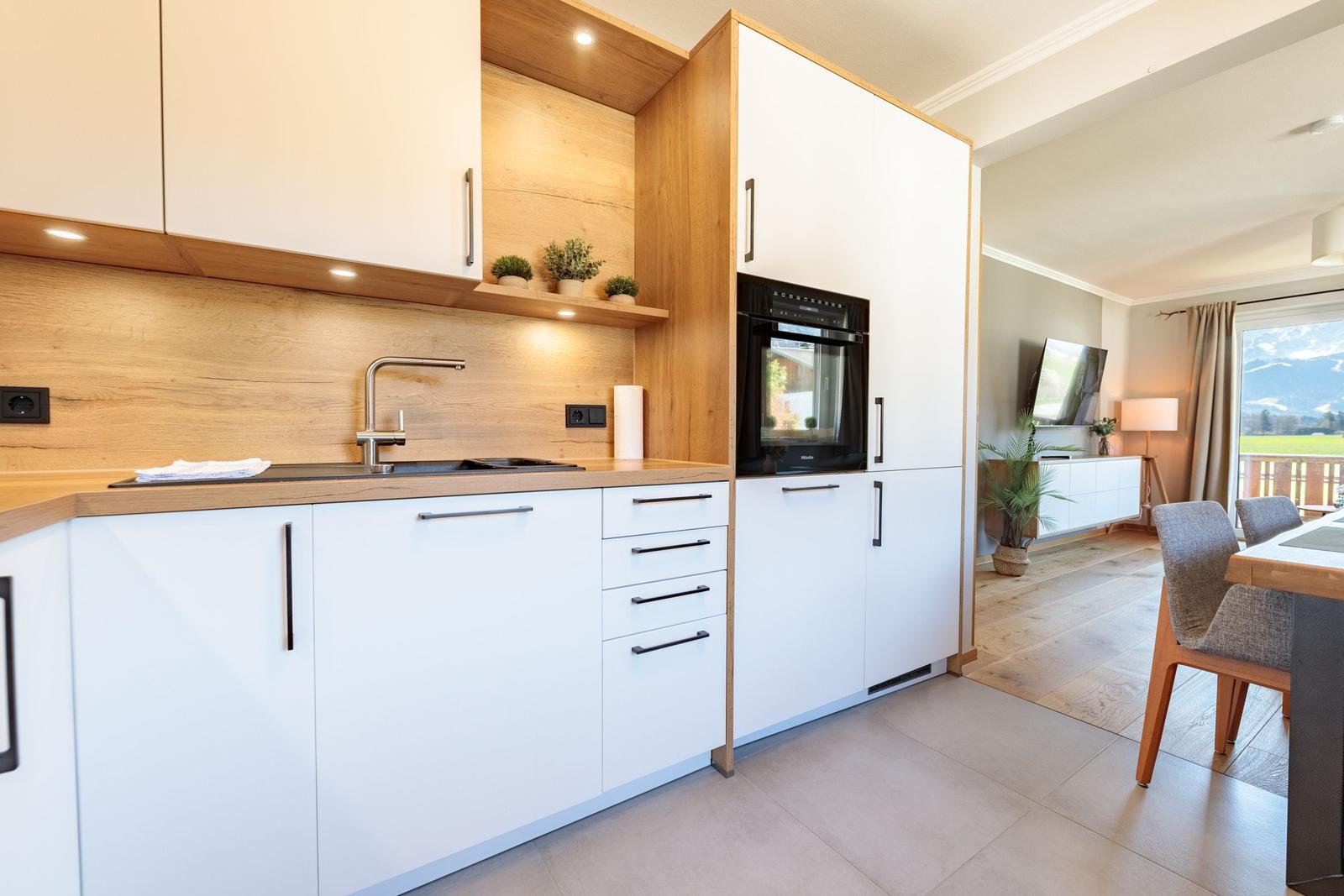 Moderne Küche mit Holzoptik und integriertem Backofen. Wohnbereich mit TV und Blick auf Landschaft.