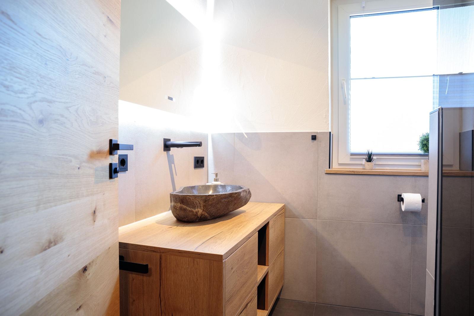 Badezimmer mit Steinwaschbecken auf Holzunterschrank und Fenster mit Pflanze.