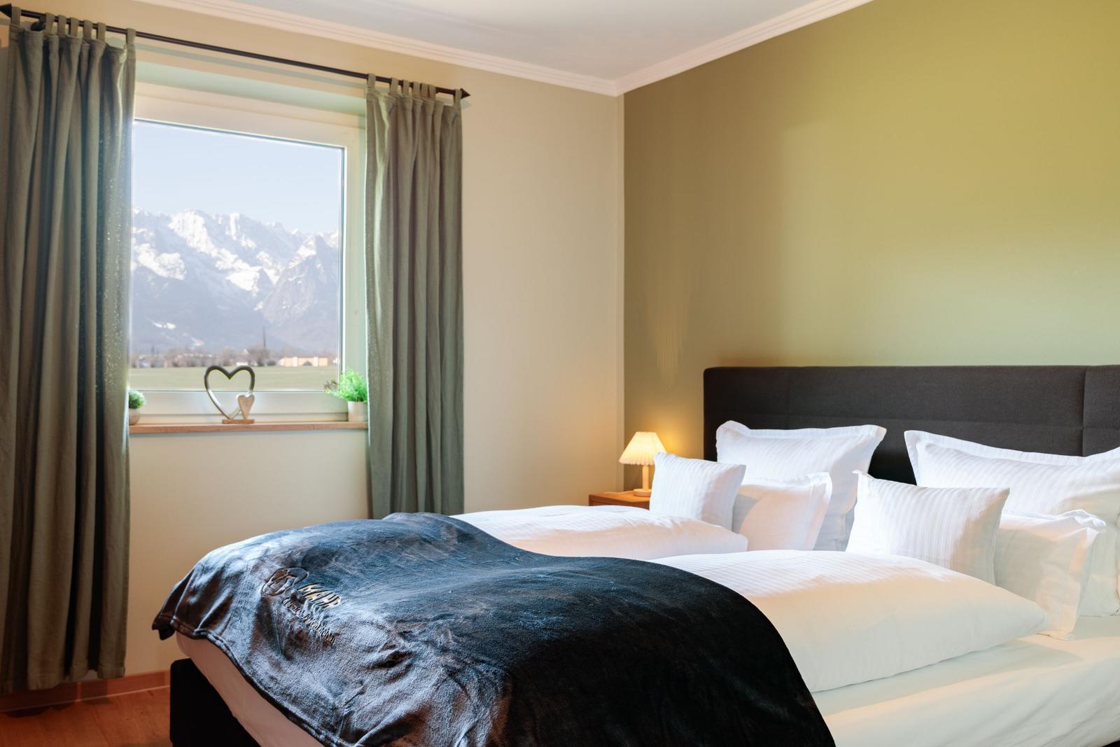 Schlafzimmer mit Blick auf Berge. Bett mit weißen Kissen und dunkler Decke.