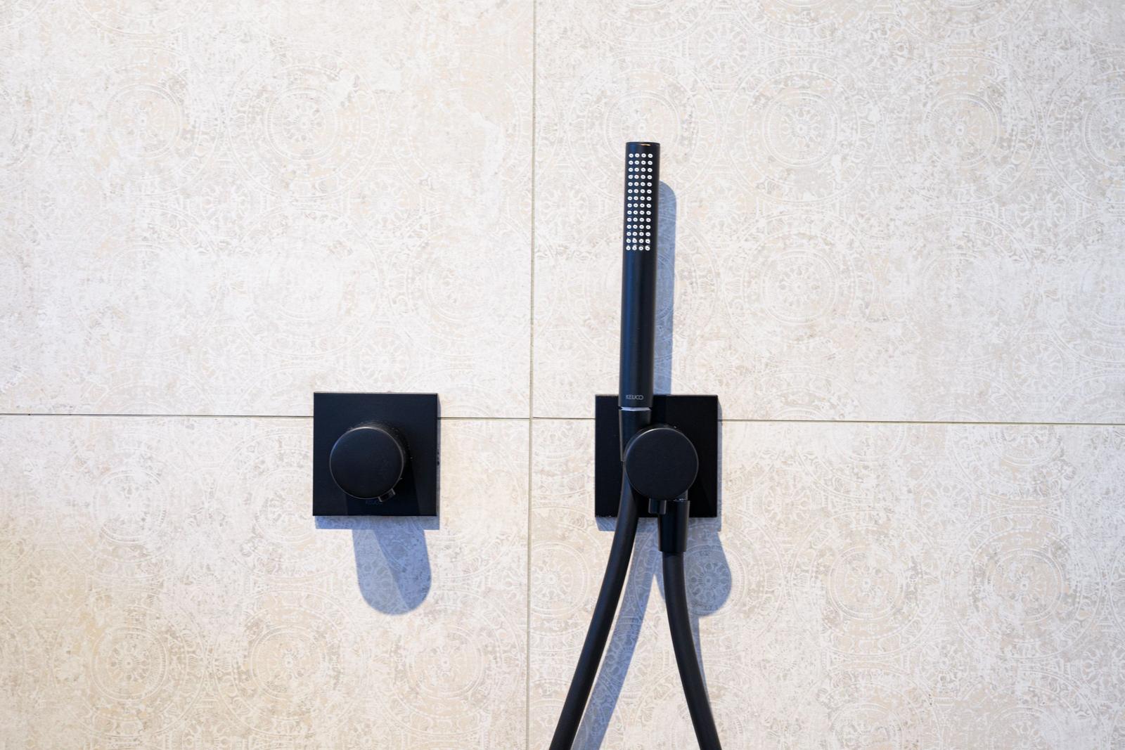 Duschkopf und Drehregler an Wand mit Mosaikfliesen
