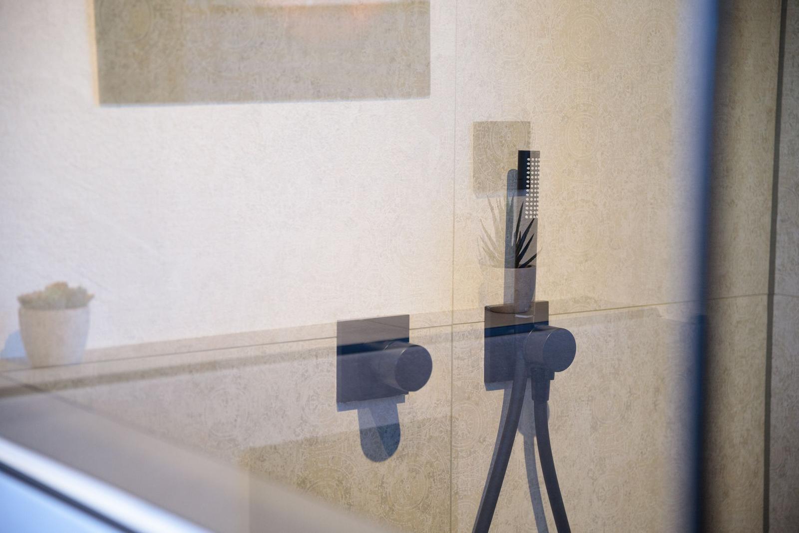 Duschkopf und Armaturen in moderner Dusche mit Glaswand und dekorativen Wänden.
