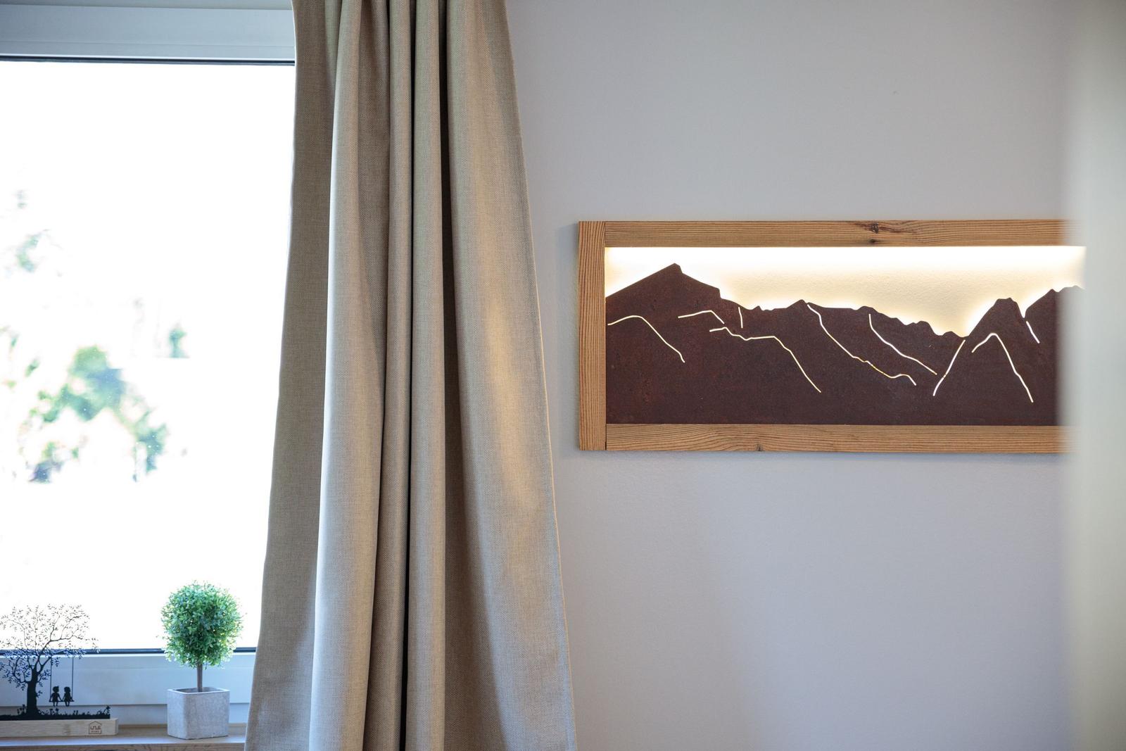Wandbild mit Bergmotiv, Vorhang und Pflanze vor Fenster