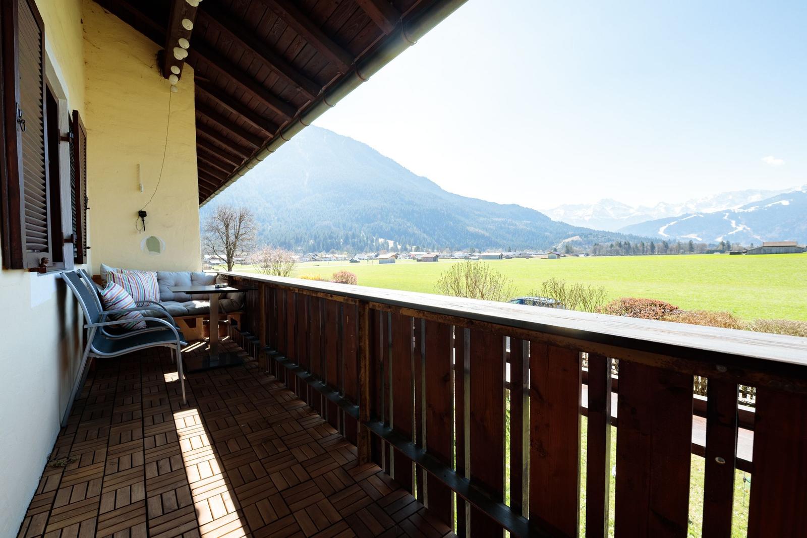 Terrasse mit Sitzgelegenheit und Blick auf grünes Feld und Berge.