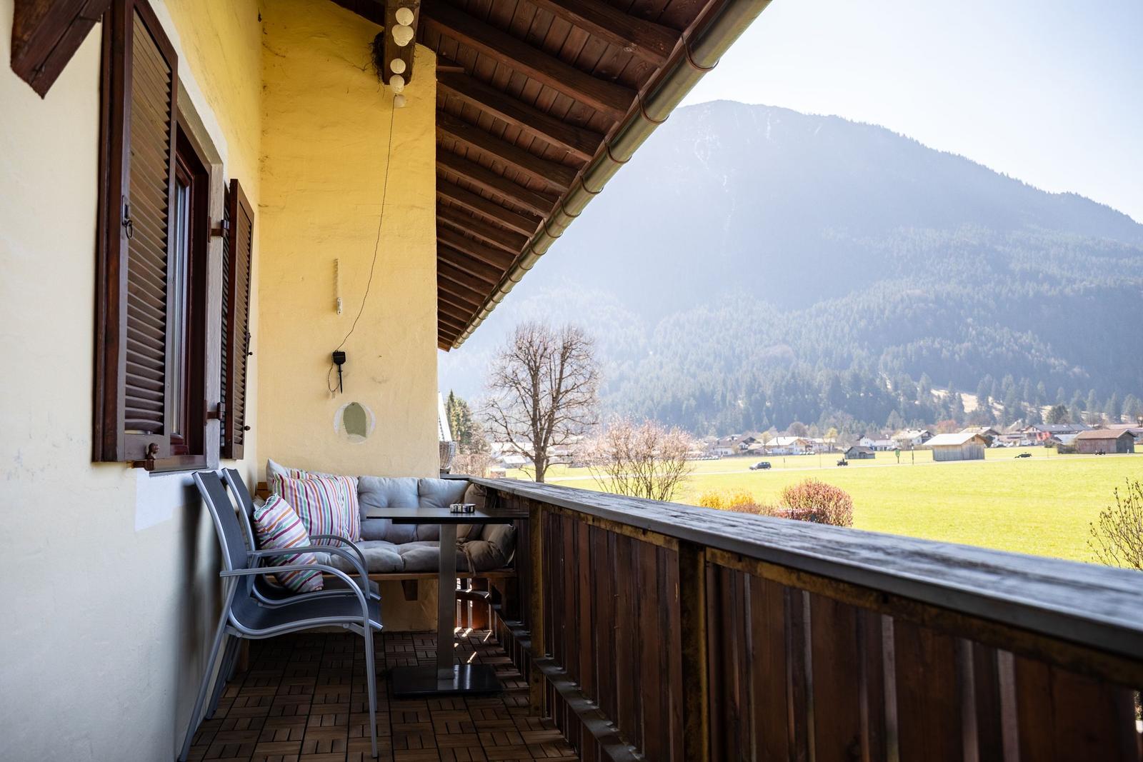 Terrasse mit Sitzgruppe und Blick auf grünes Feld und Berge.