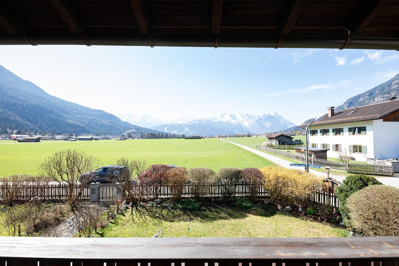 Blick von Balkon auf grünes Feld, Straße und Berge mit Schnee.