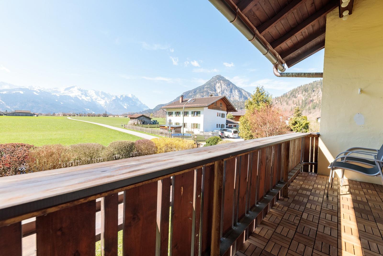 Terrasse mit Holzgeländer und Blick auf grünes Feld und Berge.