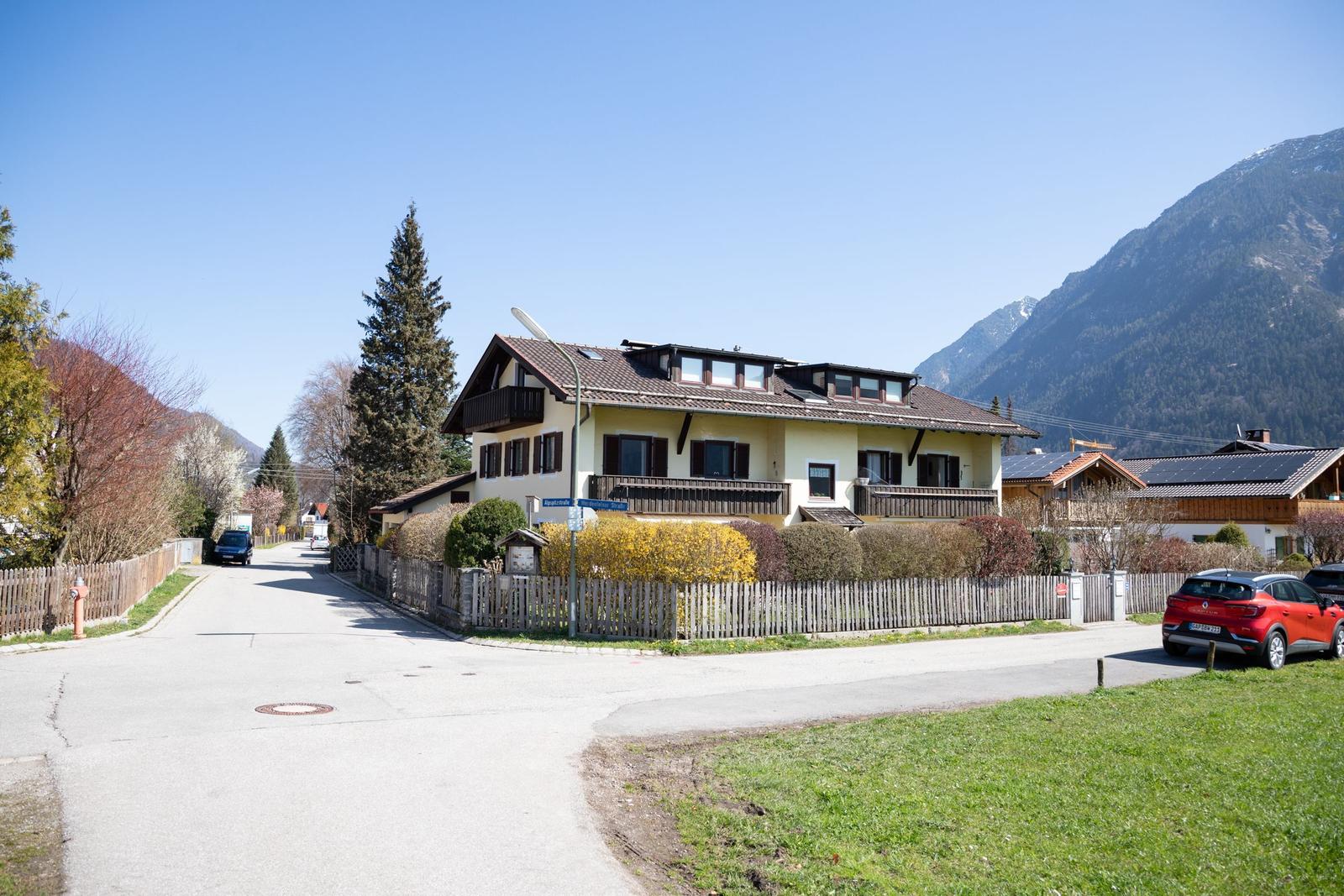 Ein zweistöckiges Haus mit Balkonen und Dachfenstern, umgeben von Grün und Bergen.