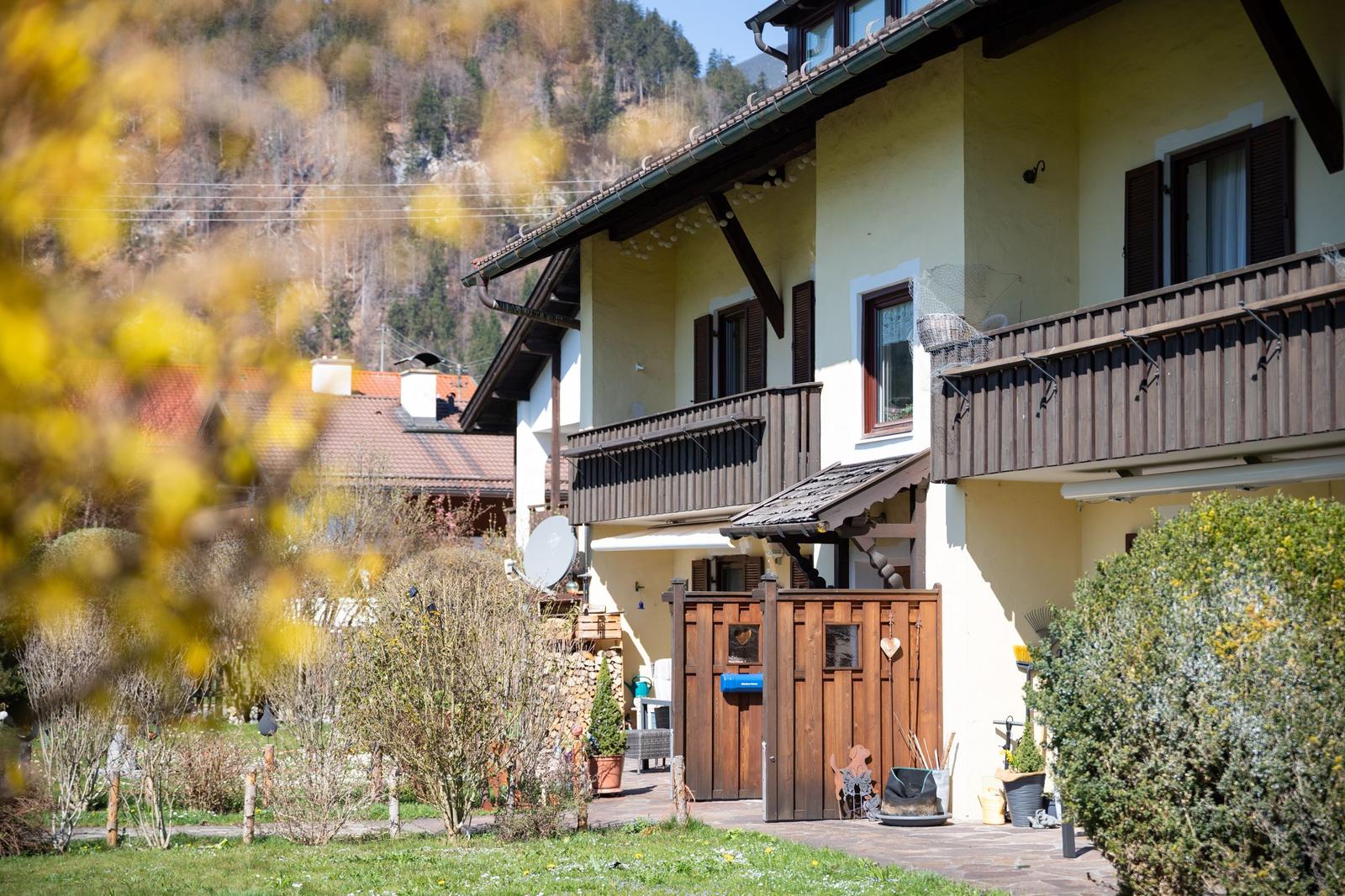 Haus mit Balkonen, Holztür und Garten. Berglandschaft im Hintergrund.